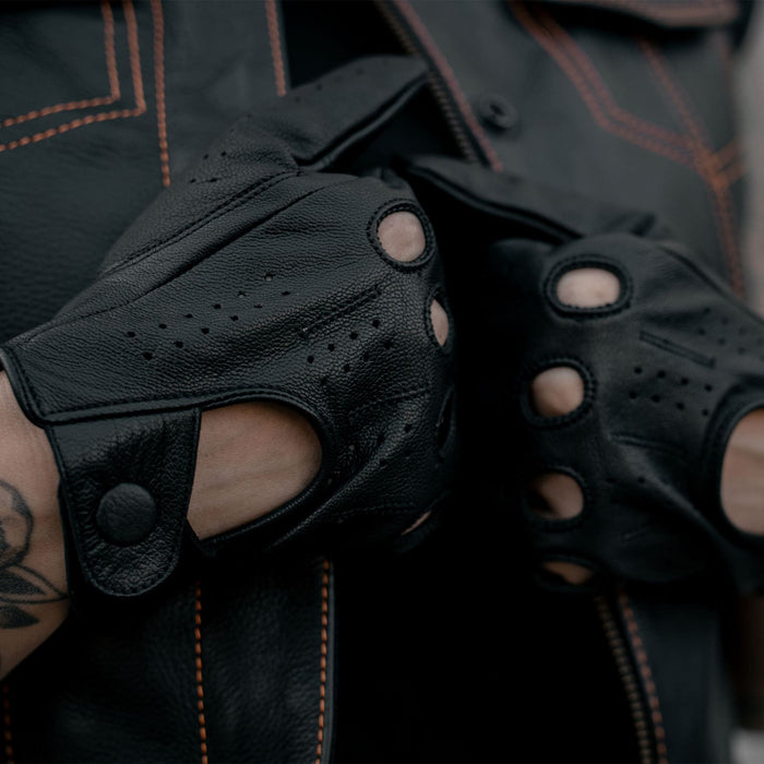 Close-up of a person wearing Leatherick black real leather driving gloves while adjusting a black leather waistcoat with orange stitching.