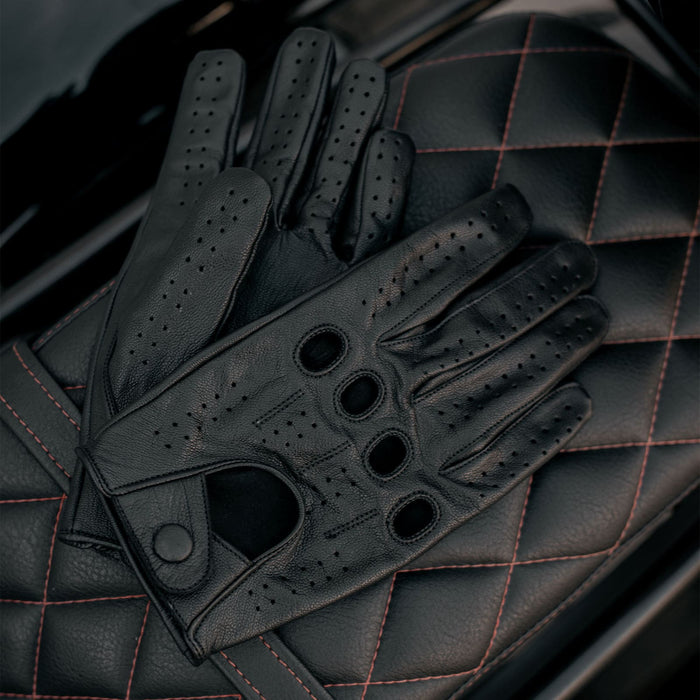 Leatherick men's black genuine leather driving gloves resting on a quilted leather motorcycle seat with red stitching.