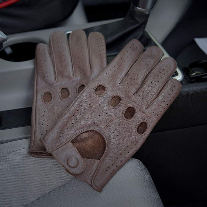 Leatherick unisex tan brown perforated leather driving gloves with knuckle holes placed on a car seat next to the gear stick.