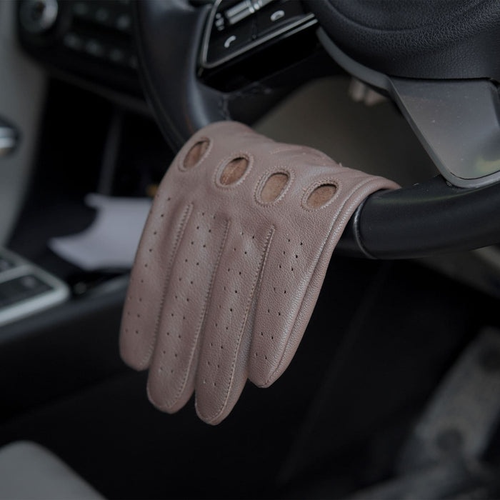 Leatherick tan brown genuine leather driving glove with knuckle holes and perforated detailing draped over a car steering wheel.